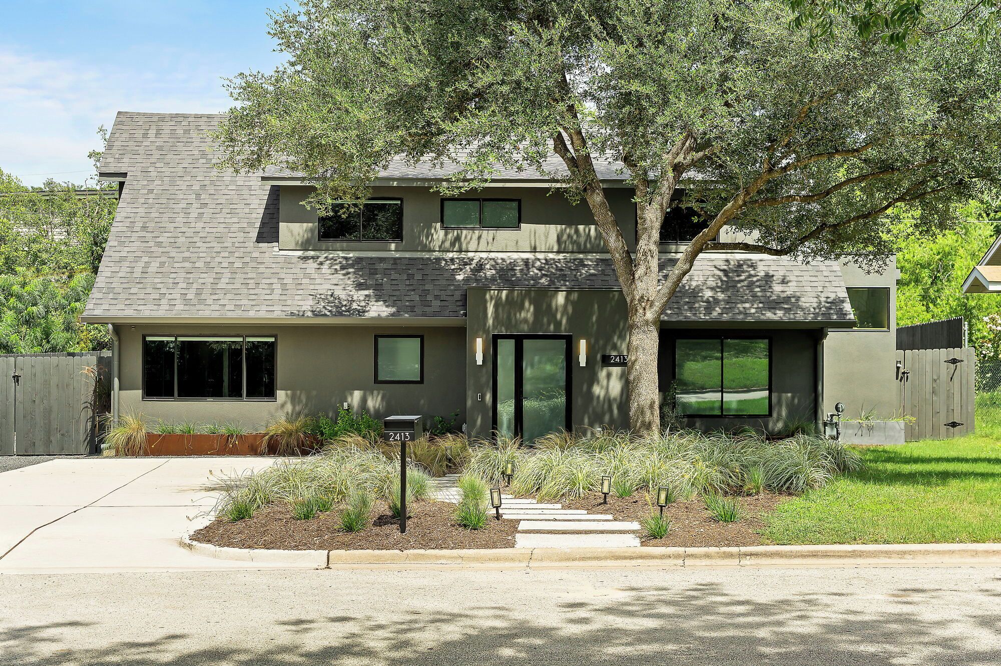 A two-story house with a modern design, featuring a large tree in the front yard and a visible mailbox.