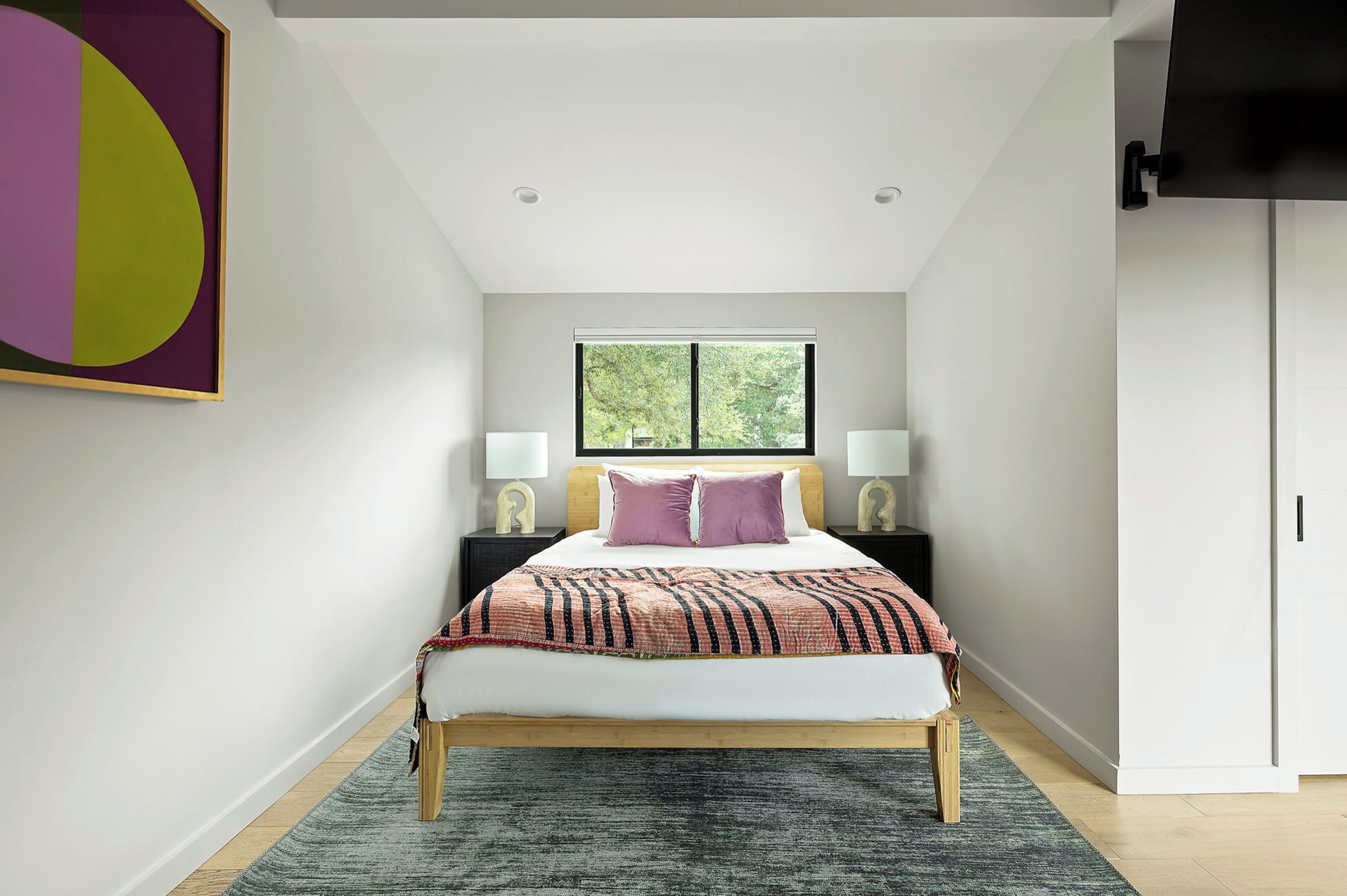 A bedroom with a bed, two bedside tables, a window, and a door.