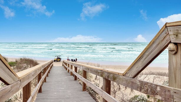Una pasarela de madera que lleva a una playa, con olas al fondo.