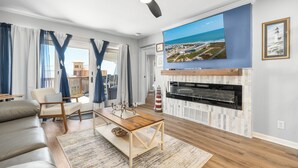 Una sala de estar con televisor grande, chimenea, sofá y vista al océano.