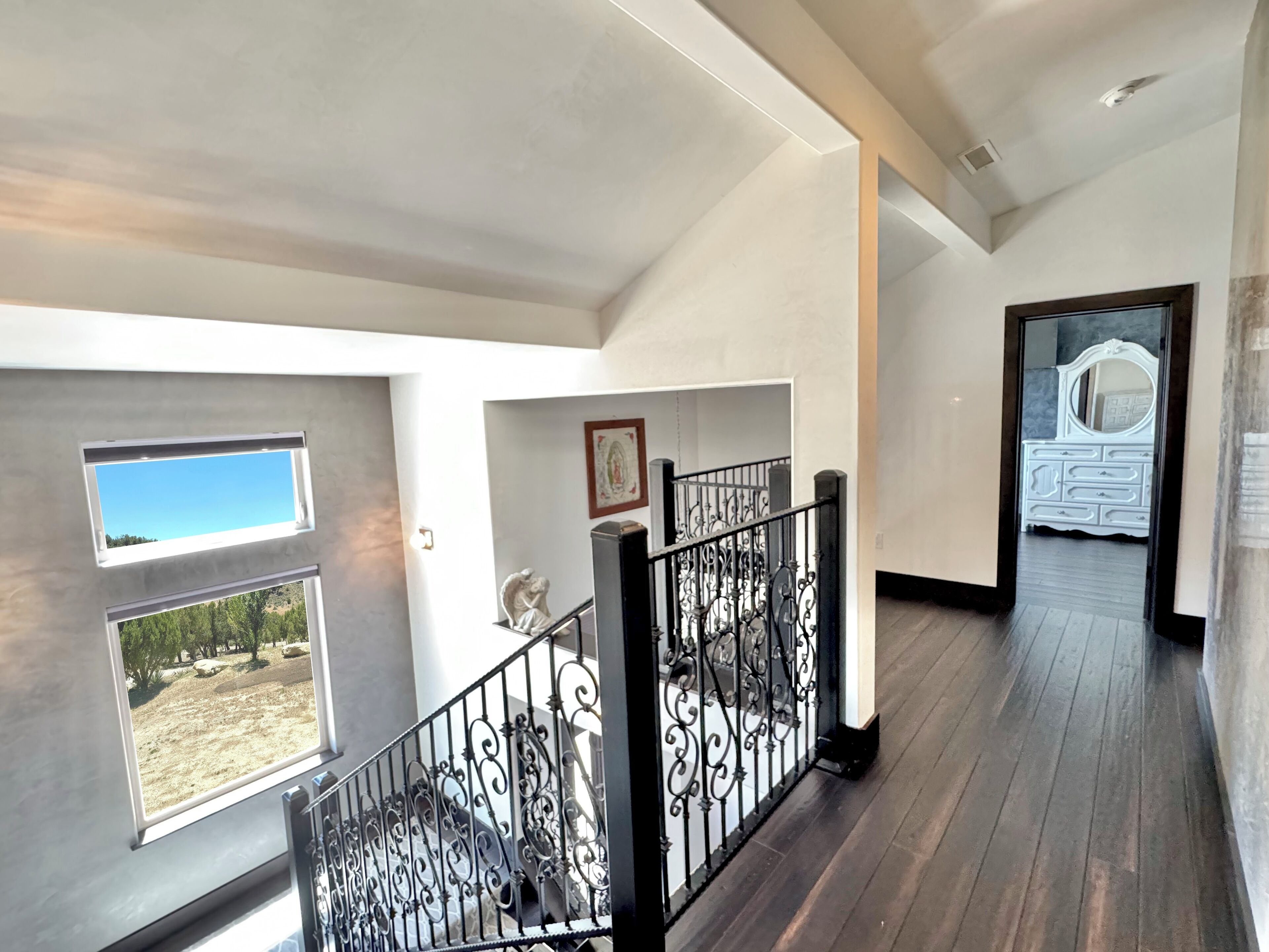 Ein geräumiger Flur mit Holzboden, einer Treppe mit aufwendigen schwarzen Geländern und einem Blick ins Freie durch ein Fenster.