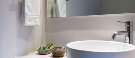 A bathroom with a white sink, a mirror, and two baskets of toiletries.