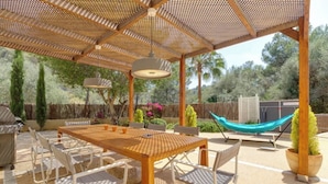 Eine Terrasse im Freien mit einem Holztisch und -stühlen, einer Hängematte und einer Pergola mit einem gewobenen Dach.