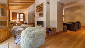 Ein geräumiges Wohnzimmer mit Holzbalkendecke, Kamin, großem Spiegel und einer gemütlichen Sitzecke mit Sofas und Poufs.