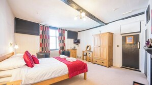 Une chambre à coucher comprenant un lit, une armoire en bois, un bureau, une chaise, un téléviseur et une fenêtre avec des rideaux.