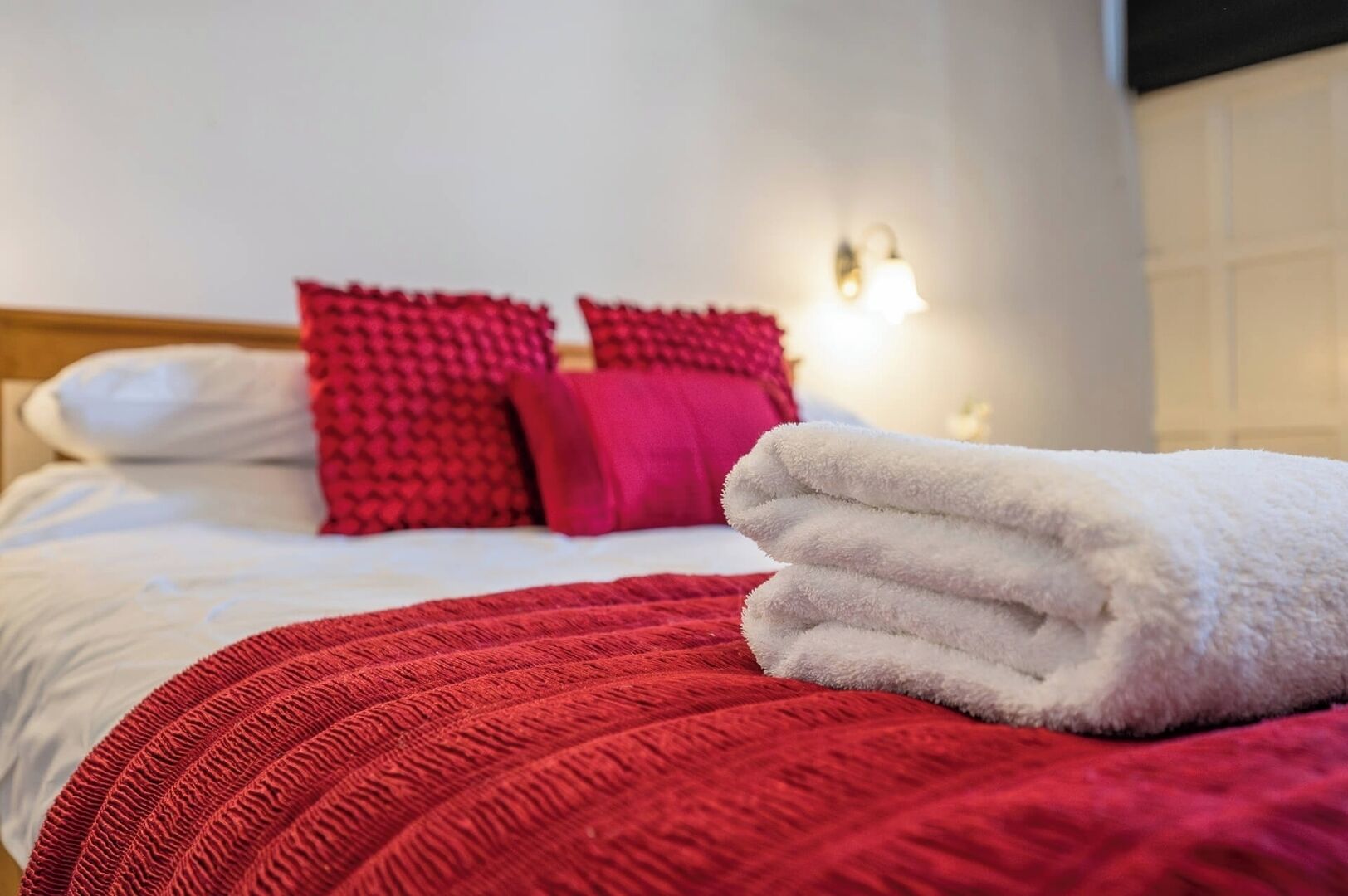 Ein ordentlich bezogenes Bett mit weißer und roter Bettwäsche, inklusive einer roten Tagesdecke und Kissen.
