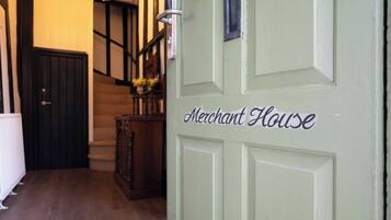 A green door with "Merchant House" written on it, a wooden staircase, and a chandelier.