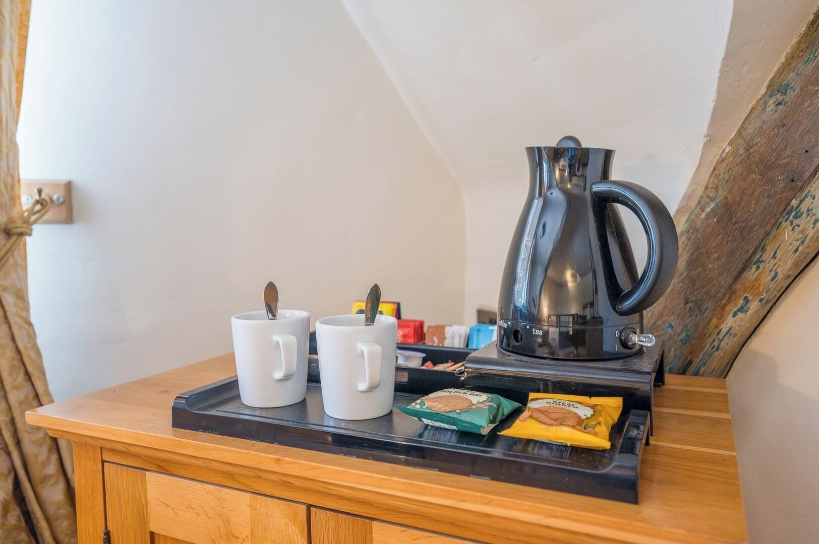 A wooden table with two white mugs, a black electric kettle, and some tea bags.