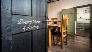 Comedor con mesa y sillas de madera, una puerta negra con el letrero "Dining Room & Puttaway" y una pared verde con un cuadro.