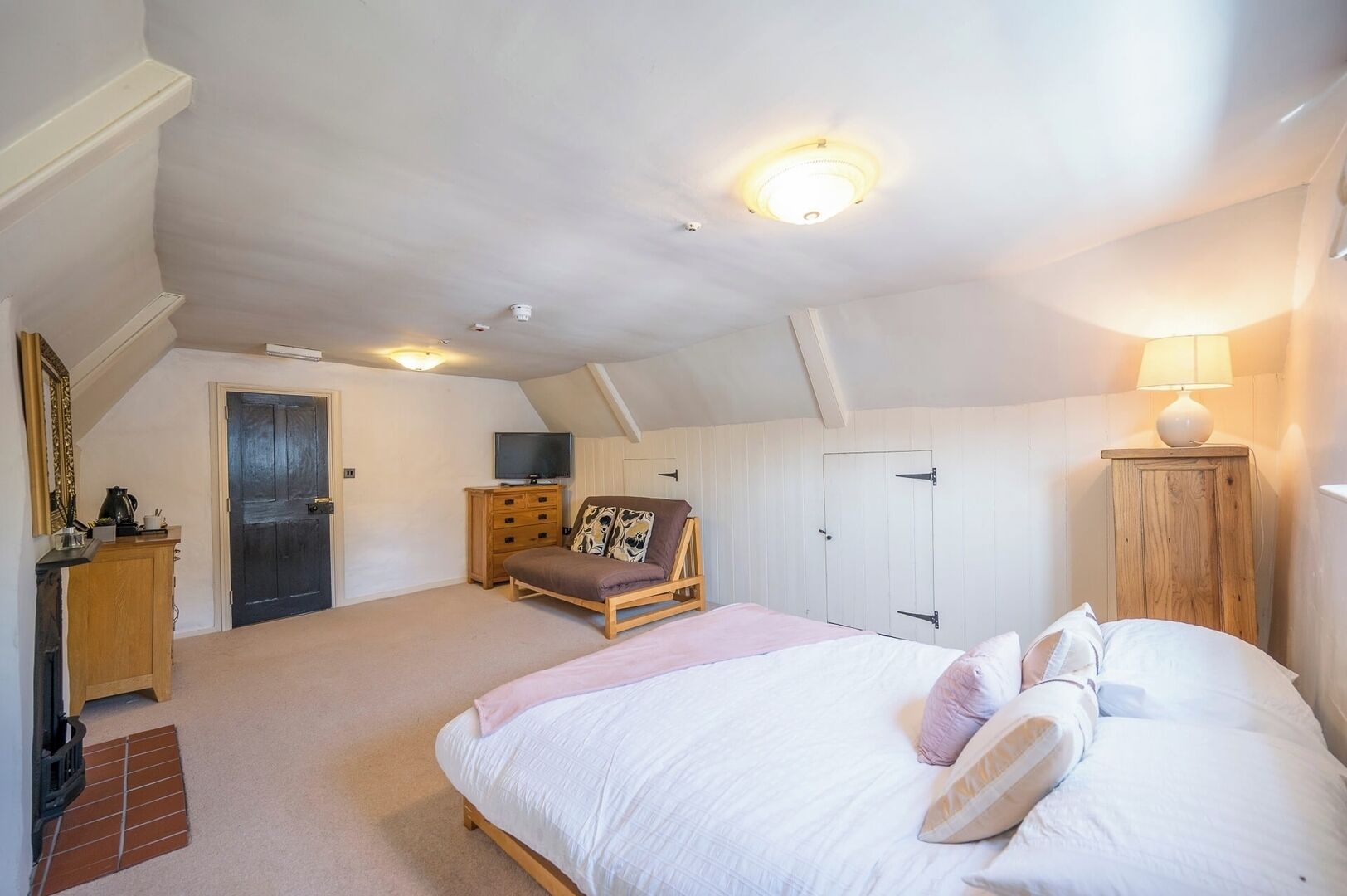 A bedroom with a large bed, a wooden dresser, a television on a stand, and a ceiling light fixture.