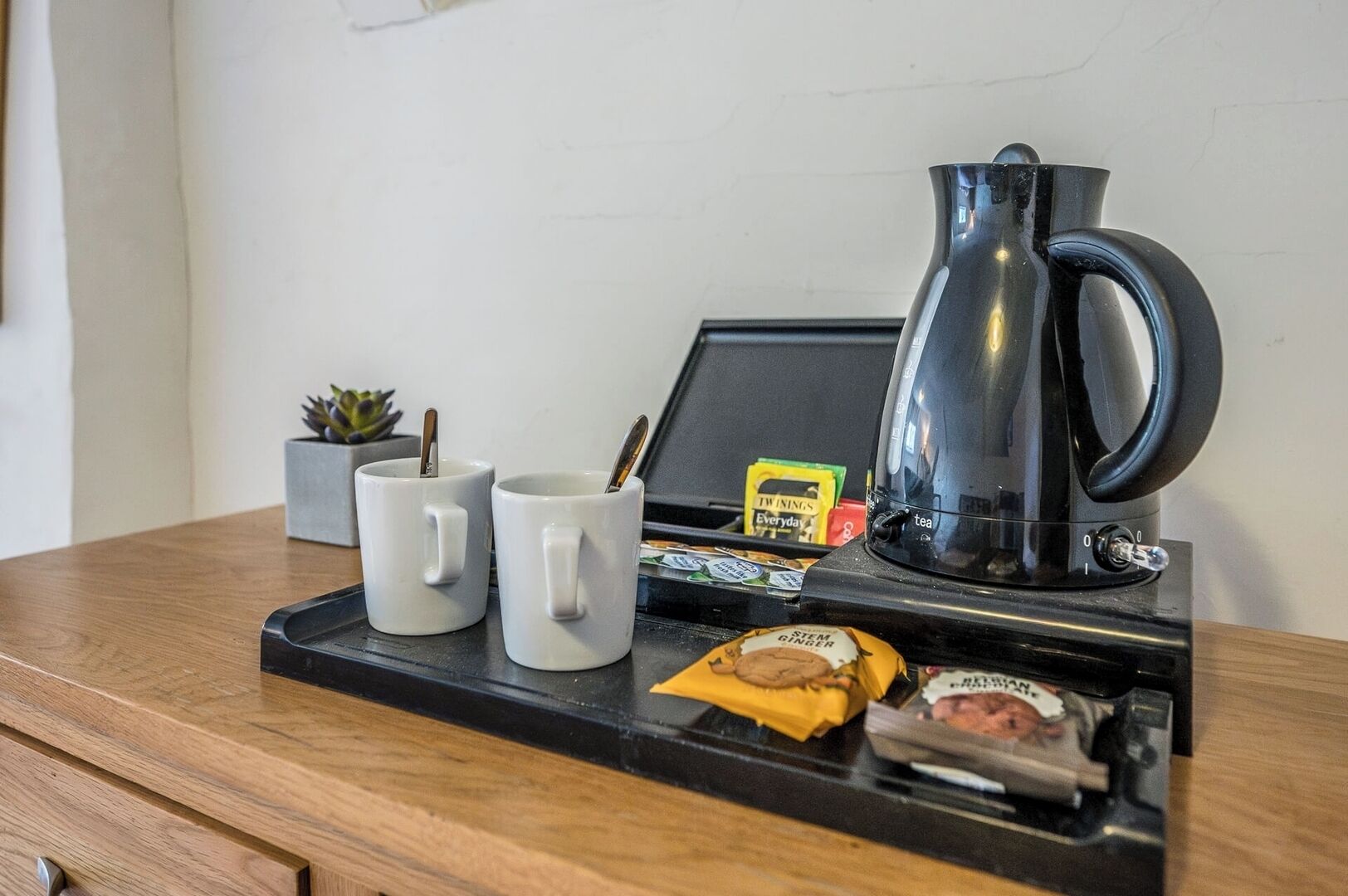 A tray with two white mugs, a black electric kettle, a small plant, and a packet of Twinings tea.