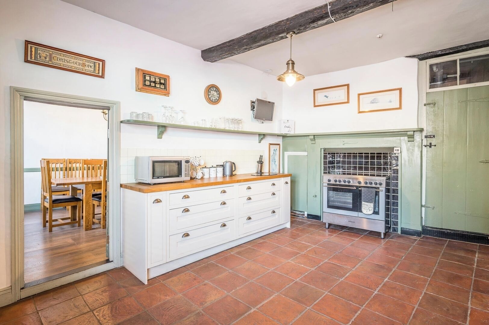 Una cocina con mesa de madera, armarios blancos, microondas y estufa antigua.