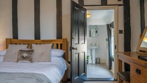 A bedroom with a wooden bed, a nightstand, and a door leading to a bathroom with a sink and mirror. - Cotton Room, The Merchant House, Ipswich (Ipswich)