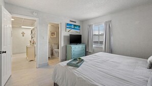 A bedroom with a bed, a television, and a window with curtains.