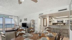 A dining area with a table set for four, a television, and a view of the ocean.
