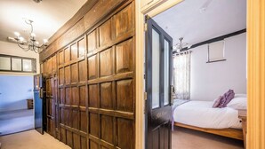 Una habitación con un armario de madera grande, una cama con colchón blanco y ropa de cama morada, y una mesita de noche pequeña.