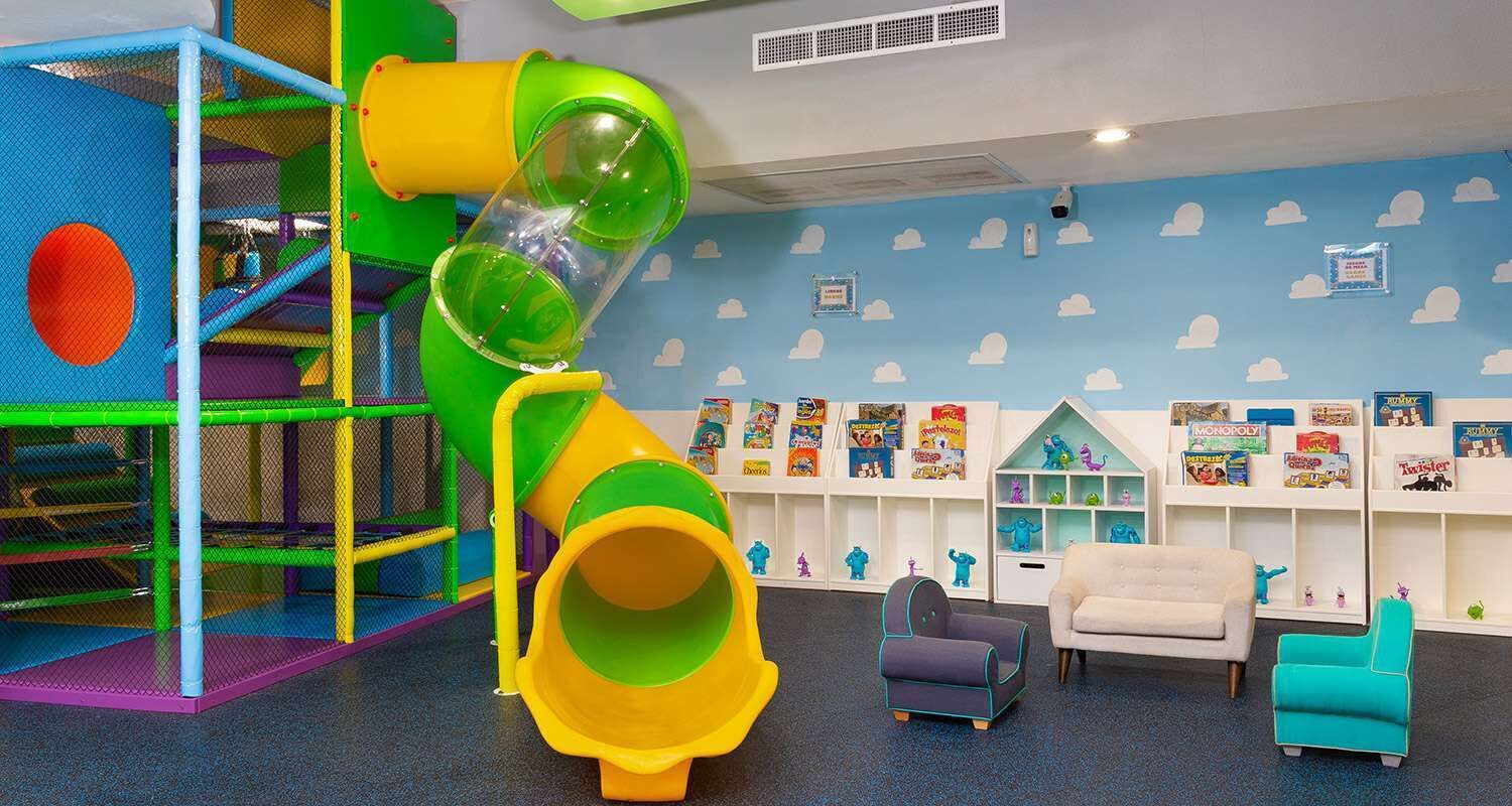 Zona de juegos infantiles con un tobogán, una estructura para escalar y una estantería con juguetes y juegos.