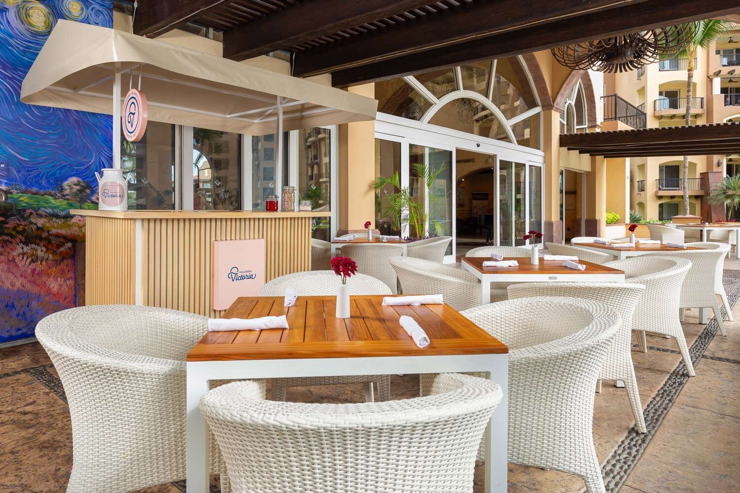 An outdoor seating area with wicker chairs and tables, a bar area with a counter, and a view of the building's interior through glass doors.