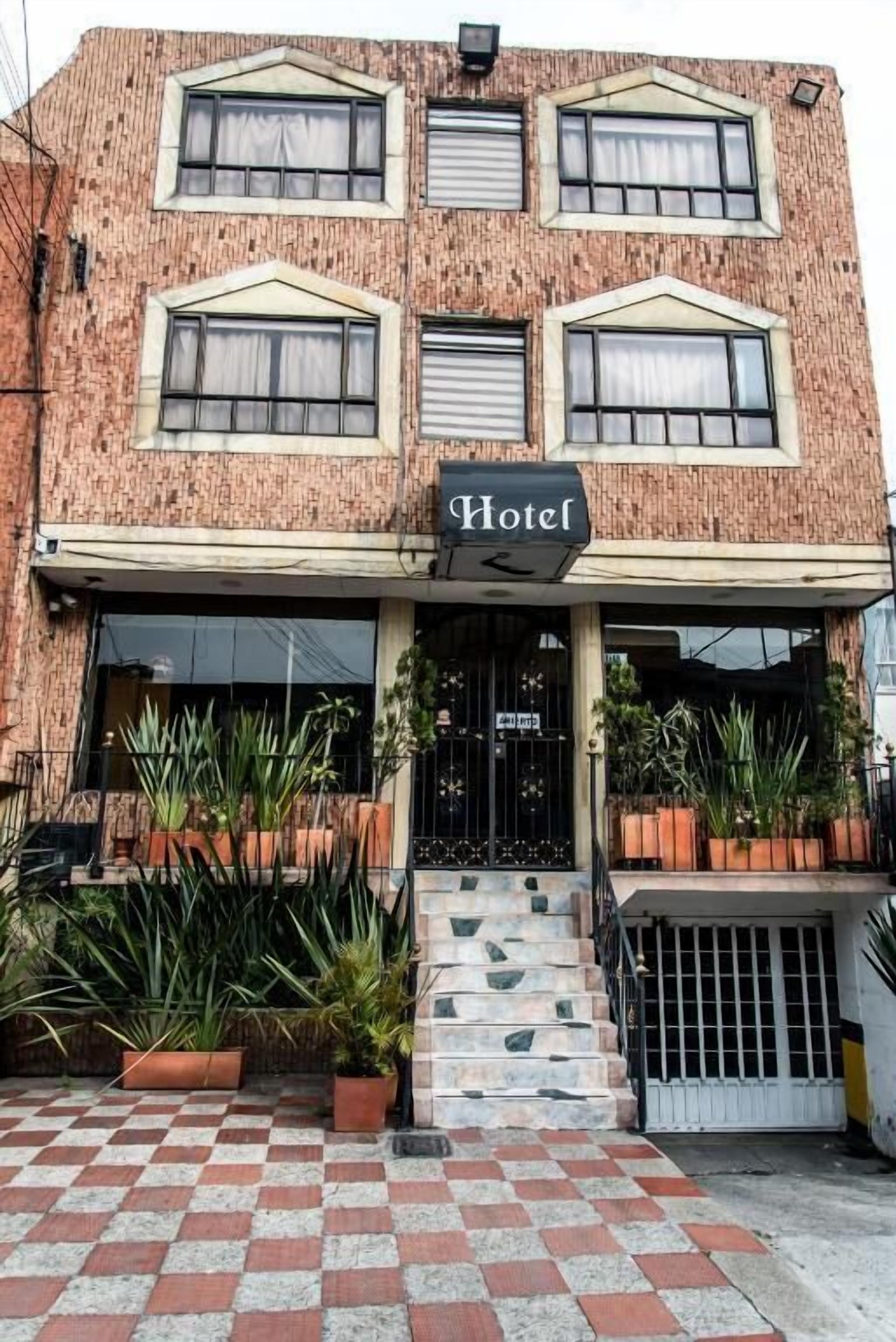 Um hotel com fachada de tijolos, chão xadrez e vasos de plantas.