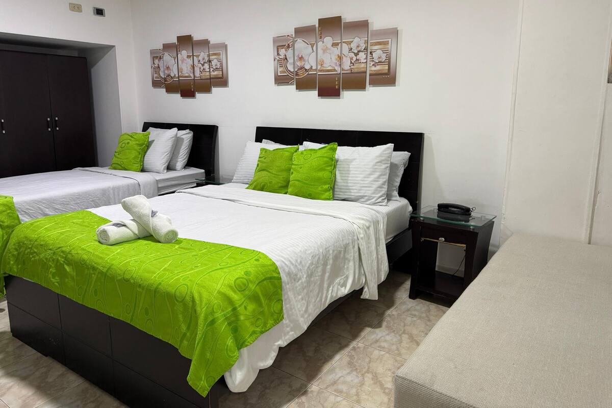 A hotel room with two beds, a wardrobe, a bedside table, and a wall-mounted artwork.