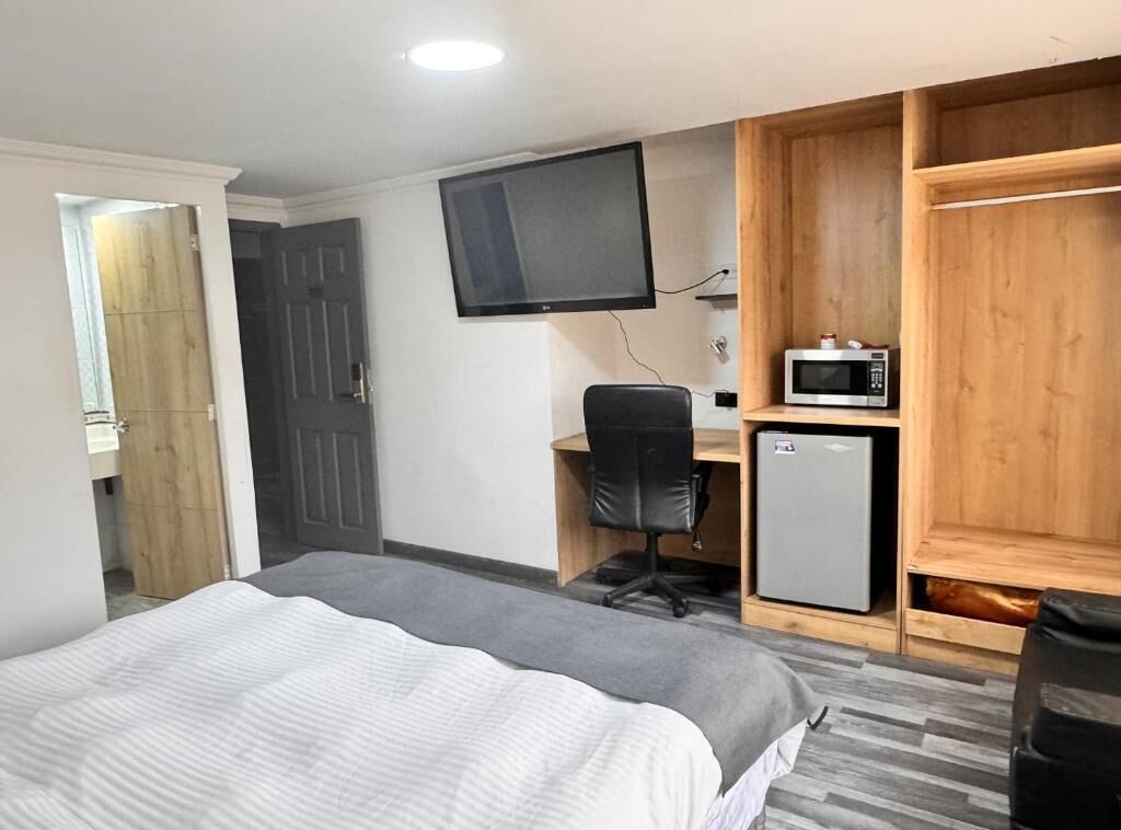 A hotel room with a bed, a desk with a chair, a television, a microwave, and a small refrigerator.