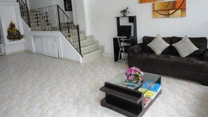 A living room with a staircase, a brown sofa, and abstract wall art. - HOTEL FENIX REAL (Bogotá)