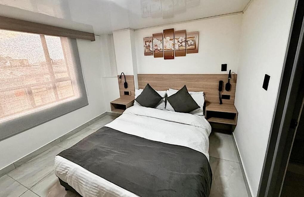 Un dormitorio moderno con una cama grande, dos mesitas de noche, un cuadro en la pared y una ventana con persianas.
