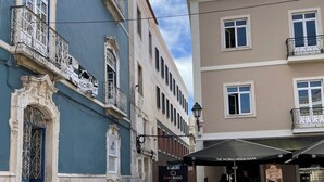 A cobblestone courtyard with outdoor seating, a blue building with ornate balconies, and a beige building with a sign for "CIVIL BLOC". - Avenue Centro Casa, Setúbal (Setúbal)