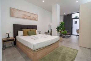 Een moderne slaapkamer met een groot bed, een nachtkastje met een lamp, een groen vloerkleed en een plant in pot.