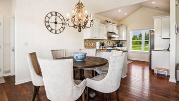 A dining area with a round table, four chairs, a wall clock, and a chandelier.