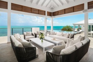 A spacious outdoor lounge area with a view of the ocean, furnished with sofas, a coffee table, and a poolside setting.