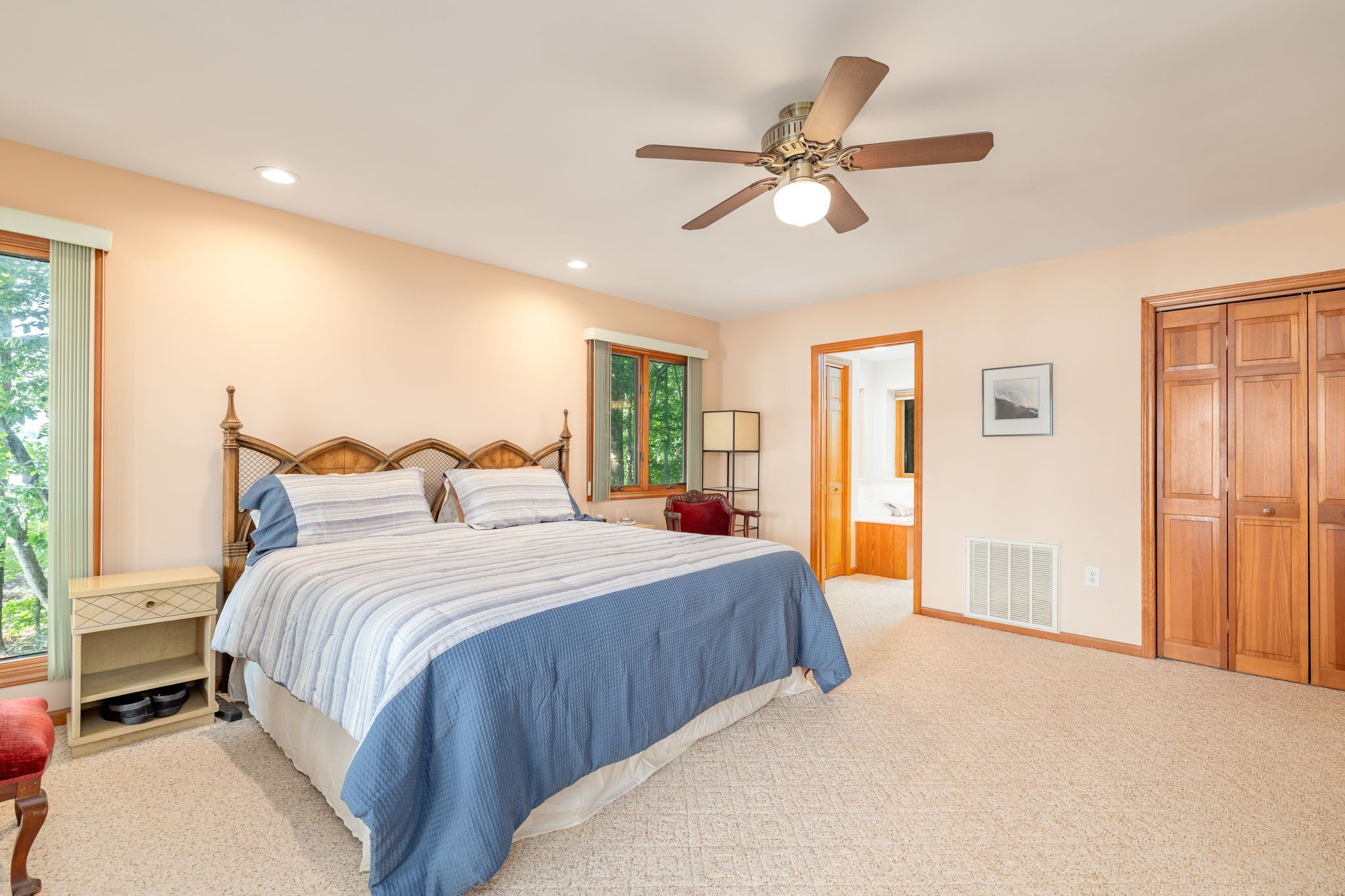 Une chambre à coucher comprenant un lit, une table de chevet, un fauteuil rouge, un ventilateur de plafond et une armoire en bois.