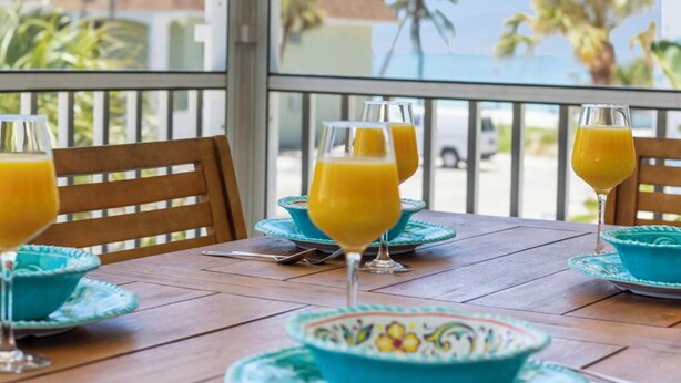A wooden table with turquoise plates and glasses of orange juice, set against a view of palm trees and a clear sky.