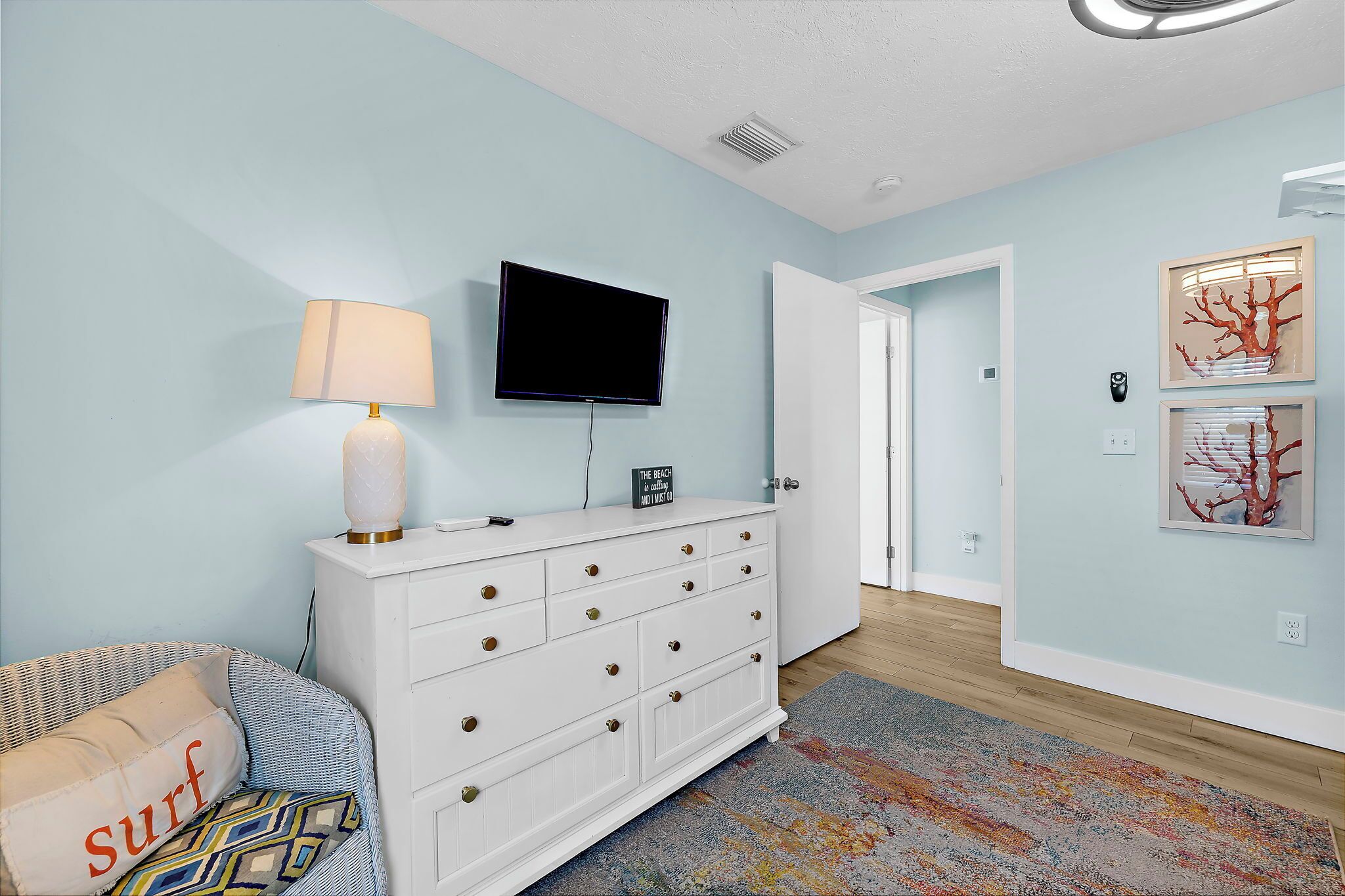 A room with a white dresser, a flat-screen TV, a lamp, and a colorful rug.