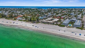 An aerial view of a coastal town with a beach, residential buildings, and a clear view of the ocean.