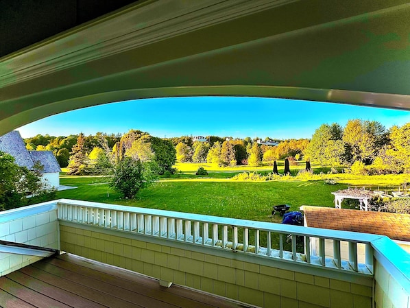 Un balcon donnant sur un paysage verdoyant, avec une clôture blanche et une terrasse en bois.
