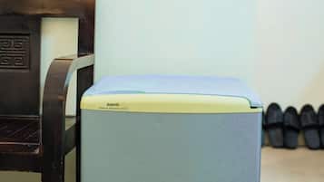 Un refrigerador pequeño azul claro con parte superior amarilla, una silla de madera y un enchufe de pared.