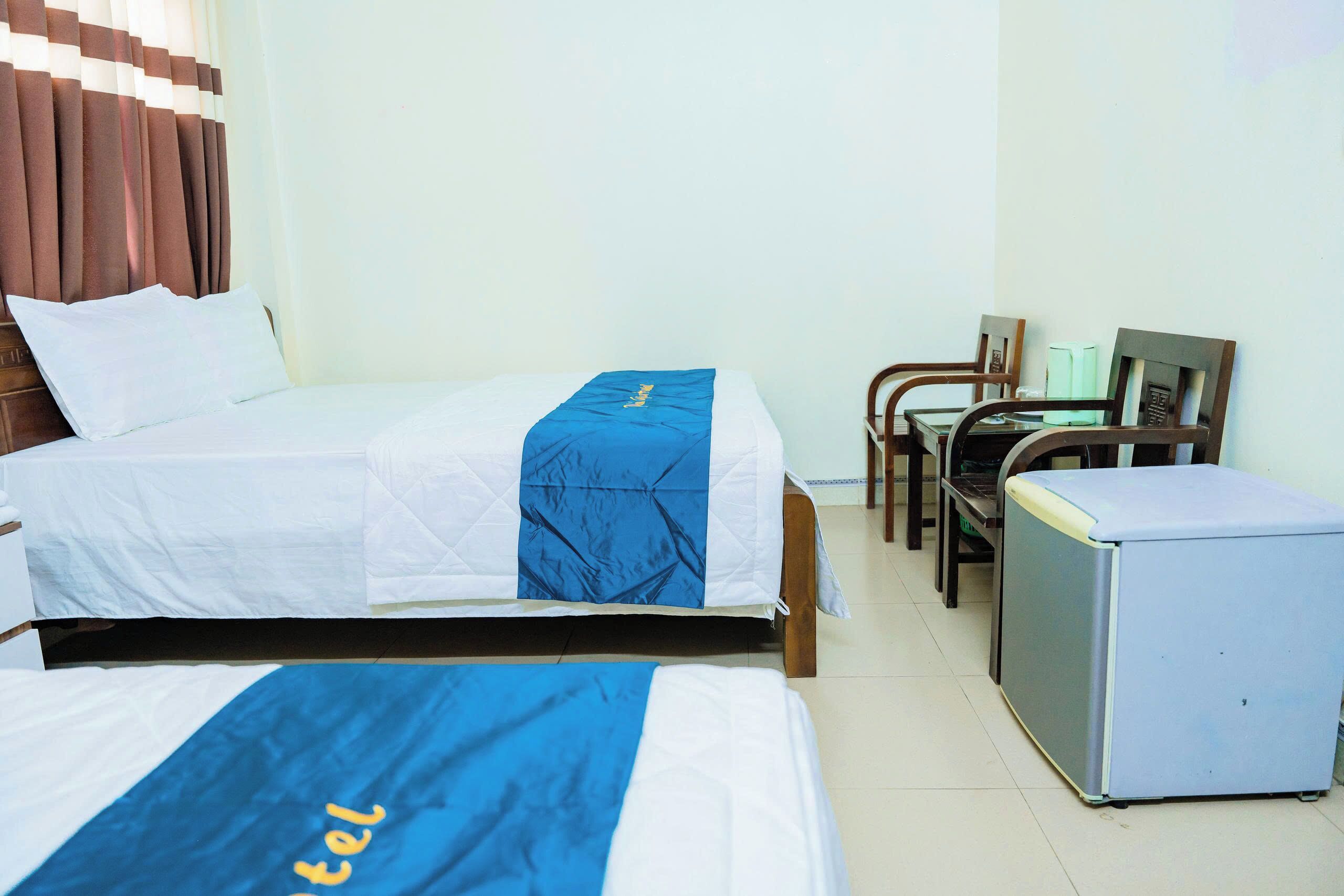 A hotel room with two beds, a desk, a chair, and a refrigerator.