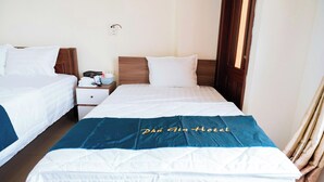Une chambre d’hôtel avec deux lits, une table de chevet avec une lampe et une fenêtre avec des rideaux.