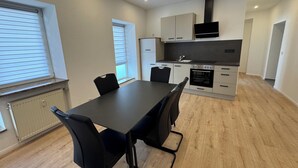 A modern kitchen with a dining table and chairs, a built-in oven, and a black range hood.