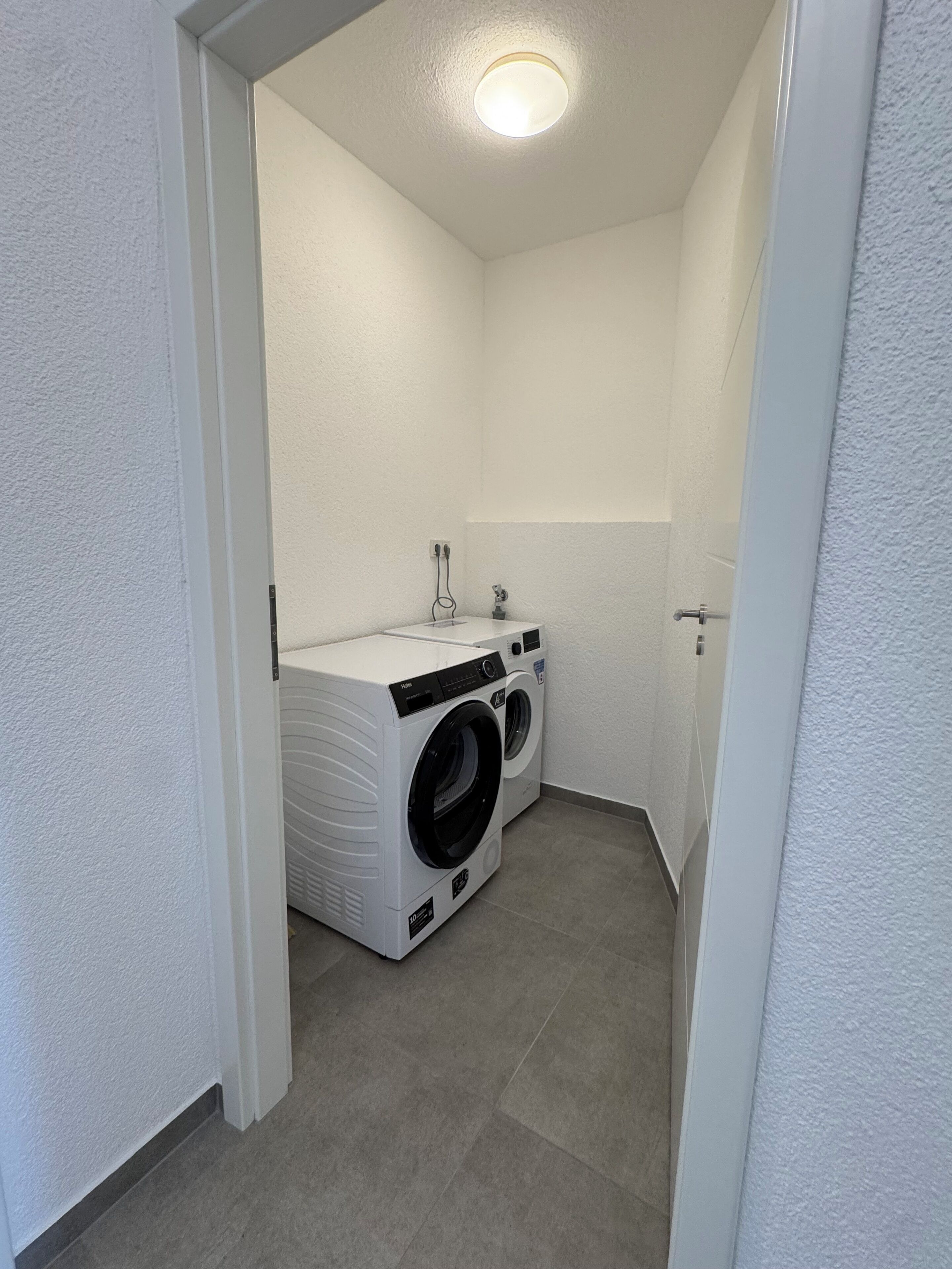 A compact laundry room with a front-loading washer and dryer, a small sink, and a towel rack.