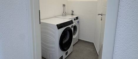 A compact laundry room with a front-loading washer and dryer, a small sink, and a towel rack.