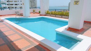 A rooftop swimming pool with a view of the ocean, surrounded by potted plants and a safety sign. - Cartagena Gem, Fully Renovated Retreat Just Minutes from Playa Hollywood (Cartagena)