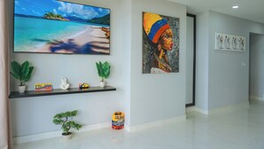 A hallway with a large flat-screen TV displaying a beach scene, a painting of a woman, and a shelf with plants and a small statue. - Cartagena Gem, Fully Renovated Retreat Just Minutes from Playa Hollywood (Cartagena)