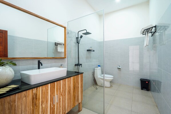 A modern bathroom with a glass shower enclosure, a white sink, and a wooden vanity. - Angseri Villas Tabanan (Penebel)