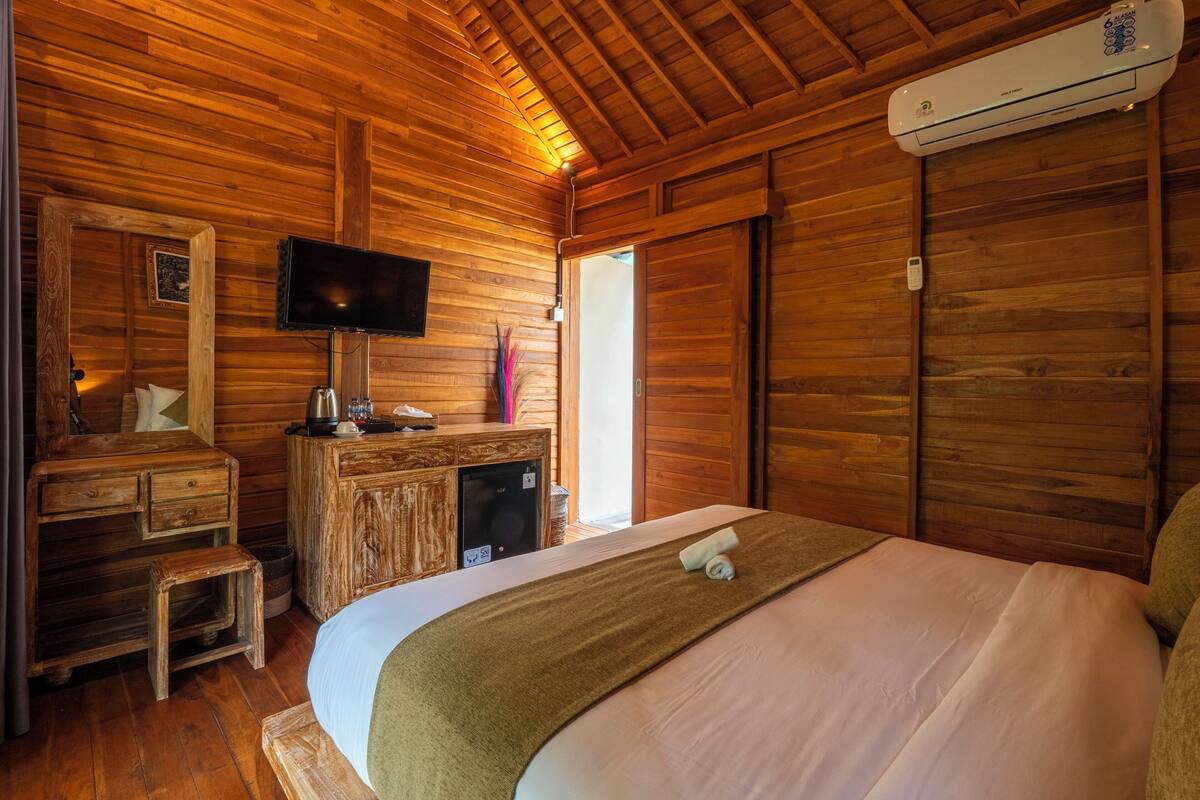 A wooden cabin room with a bed, a TV, a desk, and a wardrobe.
