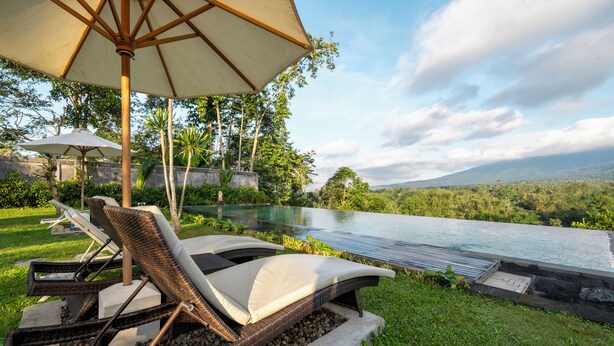 A private pool area with lounge chairs and umbrellas, surrounded by lush greenery and a view of distant mountains.