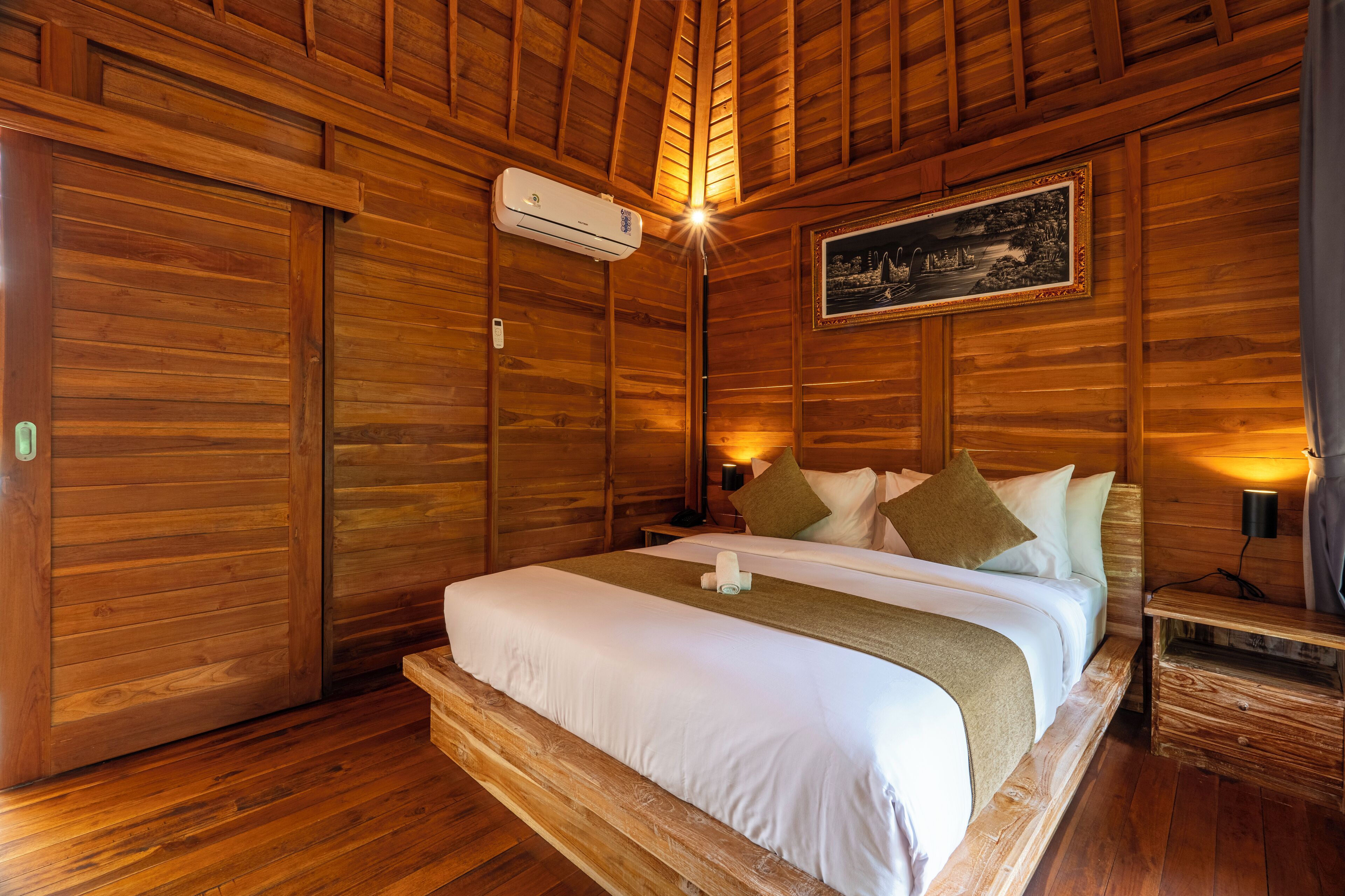 Ein Zimmer aus Holz mit einem Bett, einem Bild an der Wand und einer Klimaanlage.