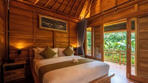 A wooden room with a bed, a nightstand, a painting, and a view of greenery outside.