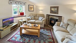 A cozy living room with a sofa, a wooden coffee table, a fireplace, and a television. - South Sandpark Cottage, Kentisbury (North Devon)